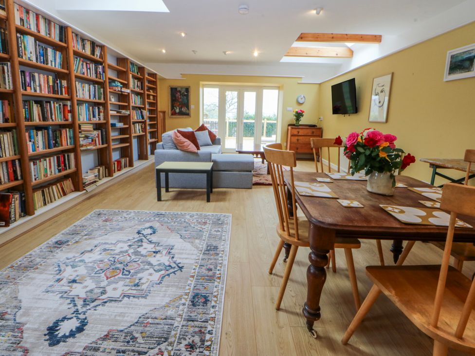 A living room with a bookshelf, sofa, and dining table at Inglewood Bach in Conwy