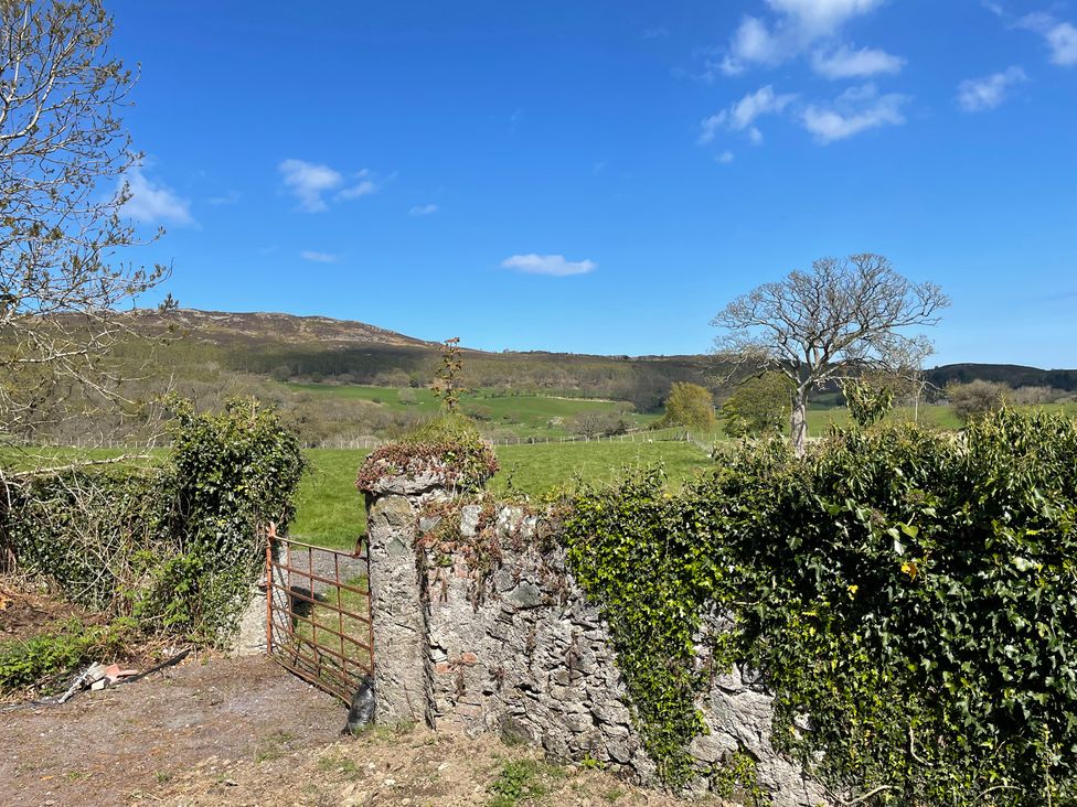 A view of a gate and stone wall with trees and hills in the background at Inglewood Bach Conwy