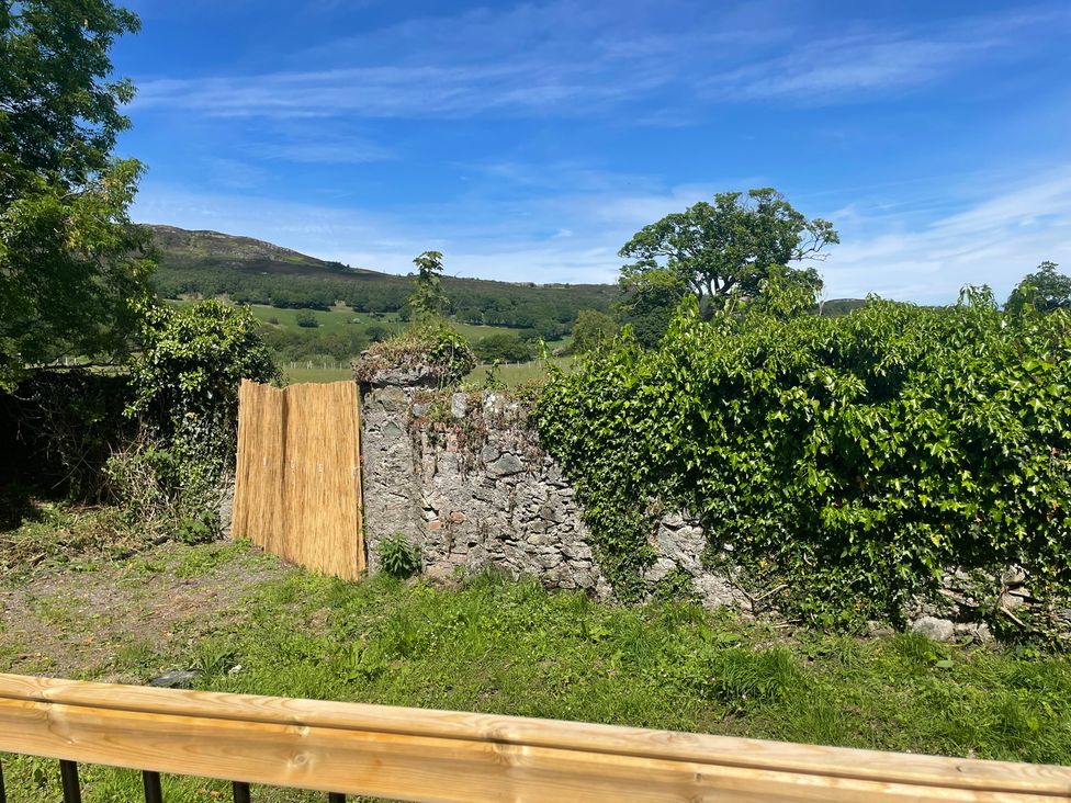 A garden with a stone wall and a wooden board at Inglewood Bach in Conwy