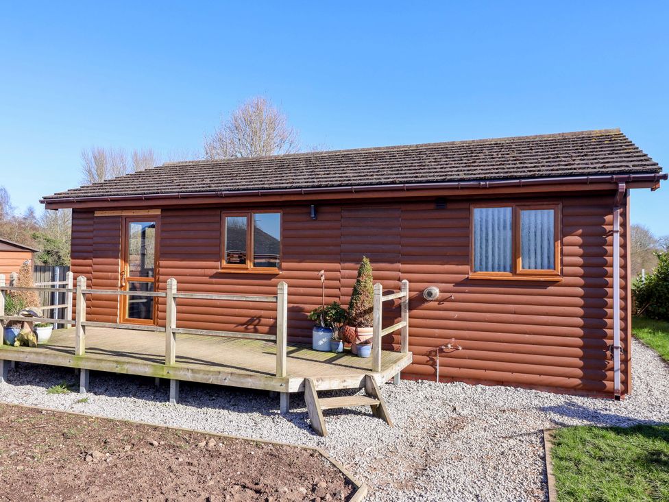 A wooden cabin with a deck and potted plants at Star Carr Lakes