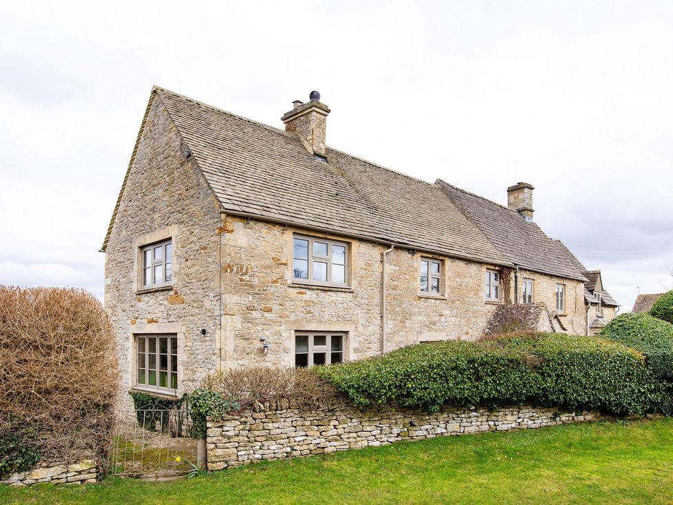 A house with windows and a stone wall at Gardeners Cottage in Chipping Norton