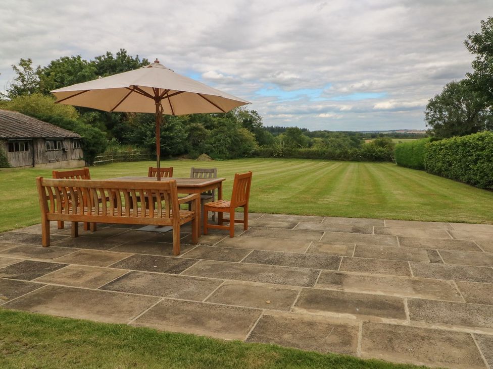 A garden with a wooden table and chairs under an umbrella at Gardeners Cottage in Chipping Norton