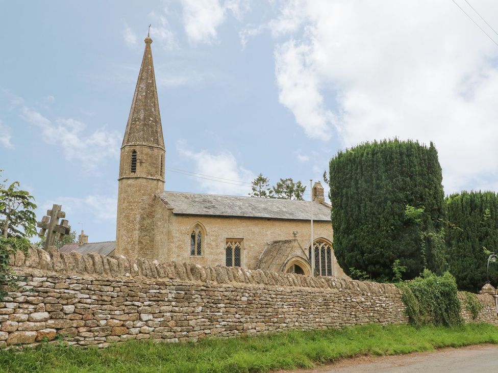 A church with a steeple and stone wall at Gardeners Cottage, Chipping Norton