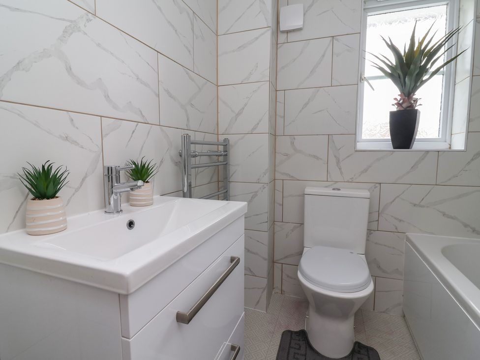 A bathroom with a sink, toilet, bathtub, and potted plants at 31 Llys Ogwen in Prestatyn