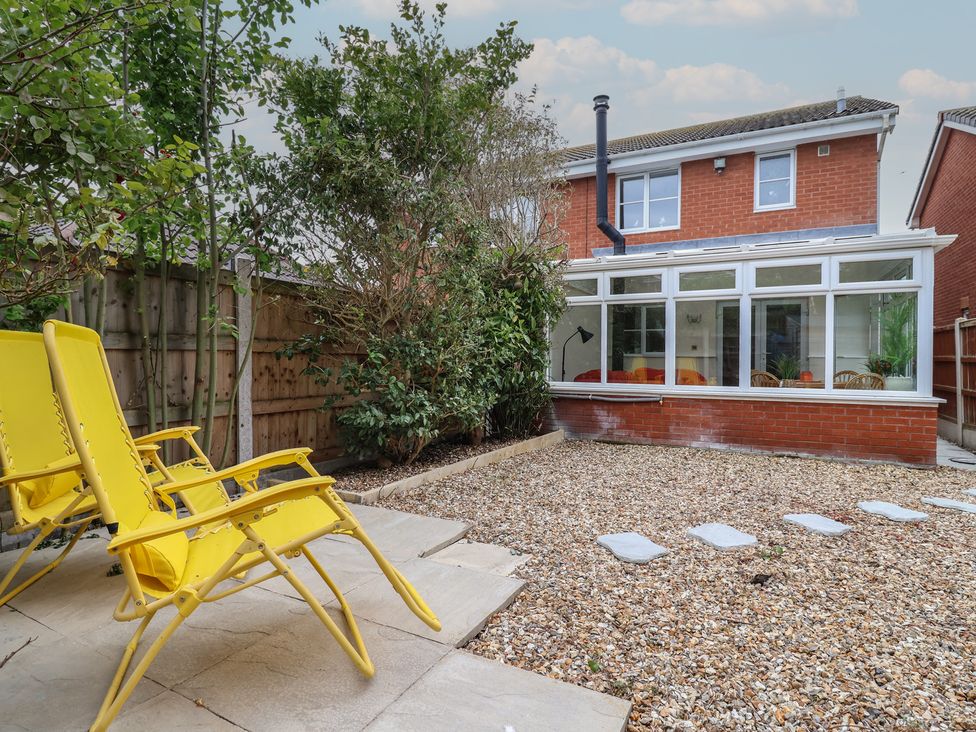 A garden with a conservatory and yellow chairs at 31 Llys Ogwen in Prestatyn