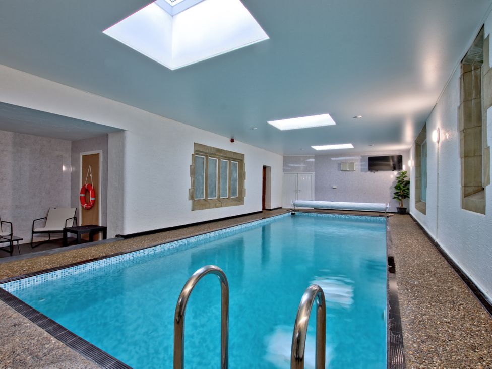 An indoor pool with lounge chairs and a television at Hanlith Hall near Malham