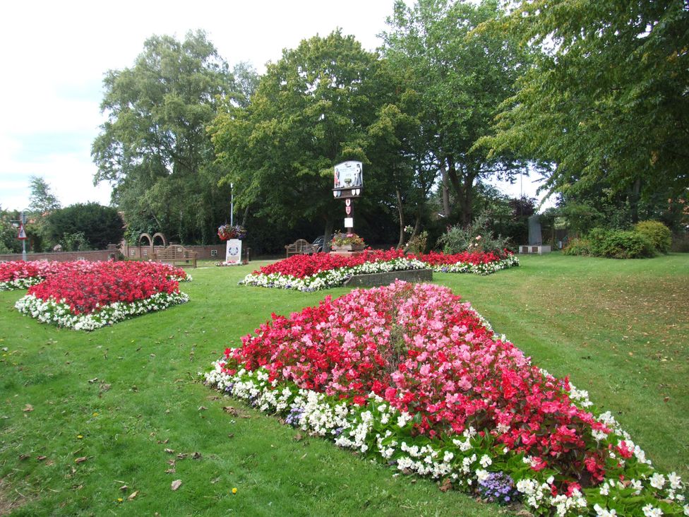 A garden area with flowerbeds and a sign at Woodland Lodge The Snug Filby