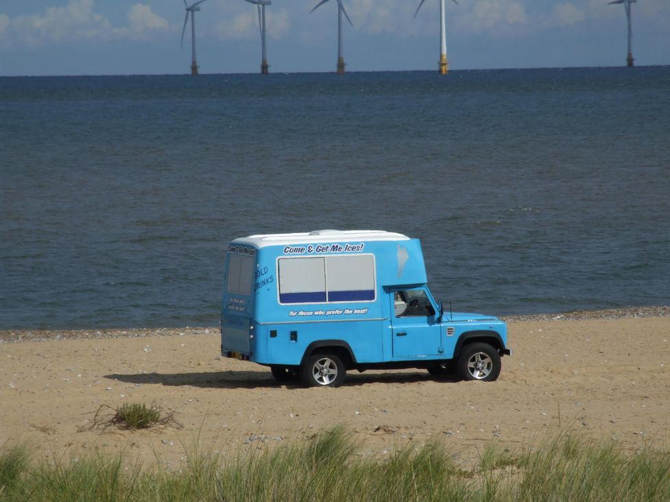 A vehicle on the beach with wind turbines in the background at Woodland Lodge The Snug Filby
