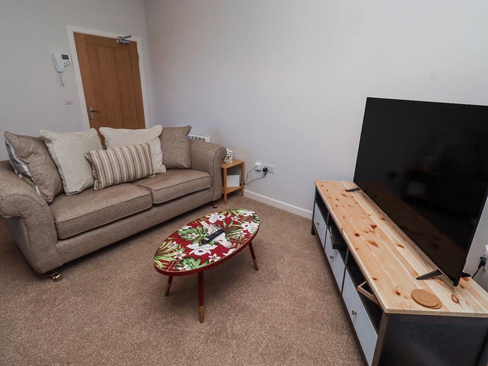 A living room with a sofa, coffee table, television, and TV stand at Amber Rose in Berwick-Upon-Tweed