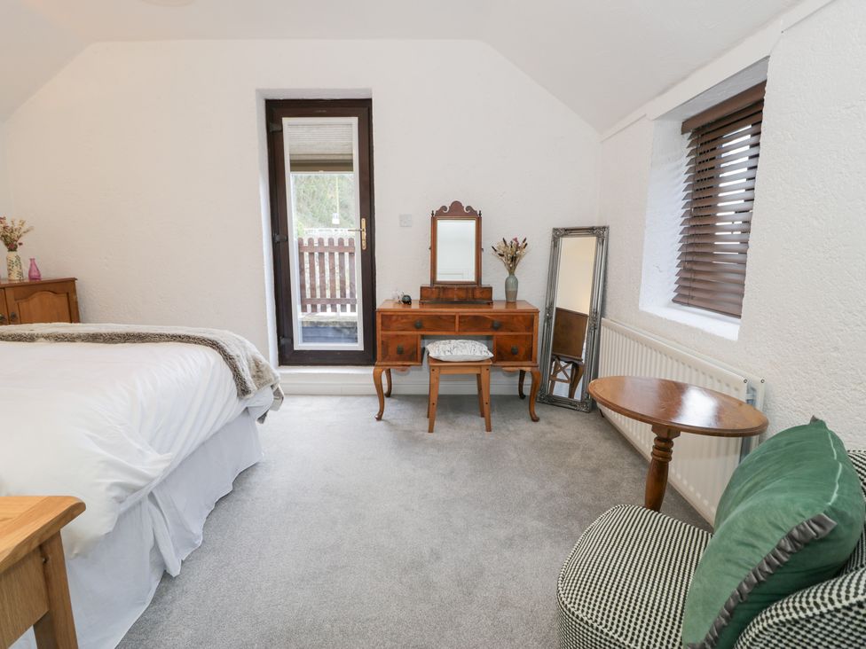 A bedroom with a bed, table, chair, and mirror at Ivy Cottage in Abergele