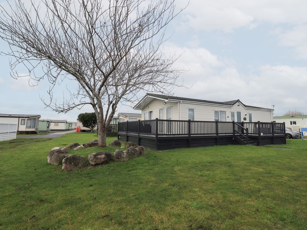 A mobile home with a wooden deck and a tree in the outdoor area at Lily's Lodge in Morecambe