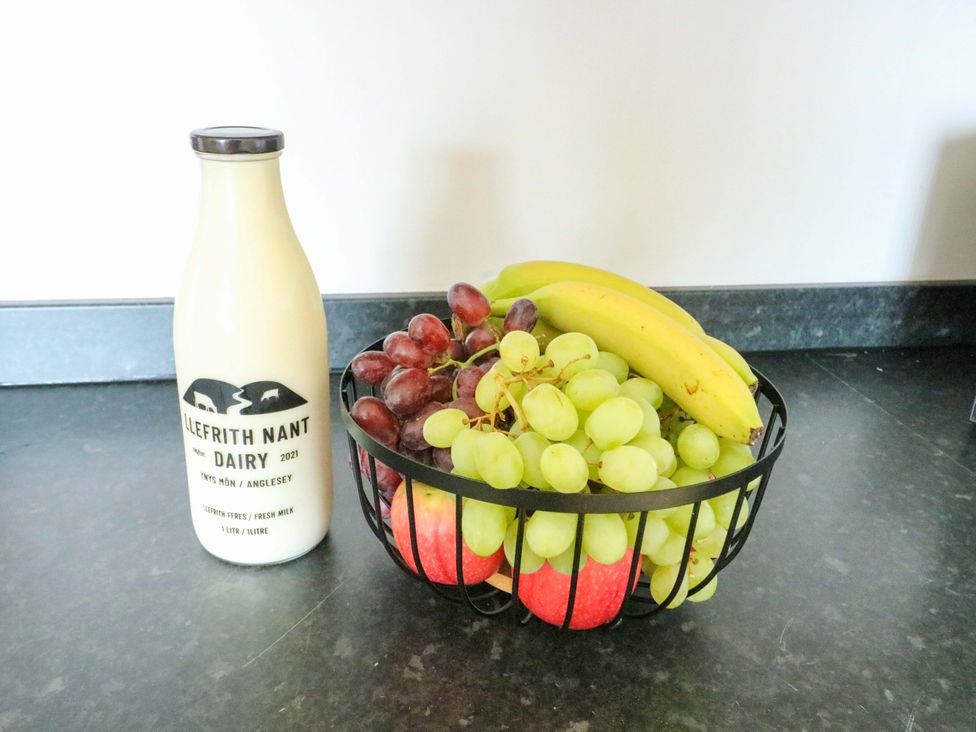 A bowl of fruit with apples, grapes, and bananas next to a milk bottle at Min Y Cae