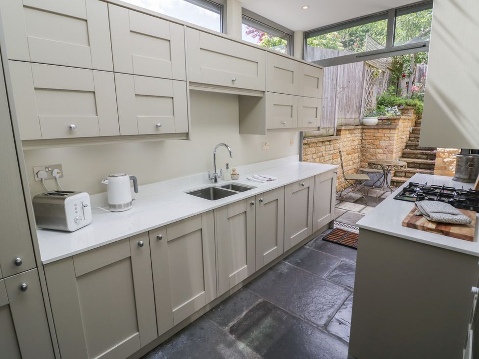 A kitchen with cabinets, sink, kettle, and view of an outdoor area at Tea Tree Cottage in Chipping Campden