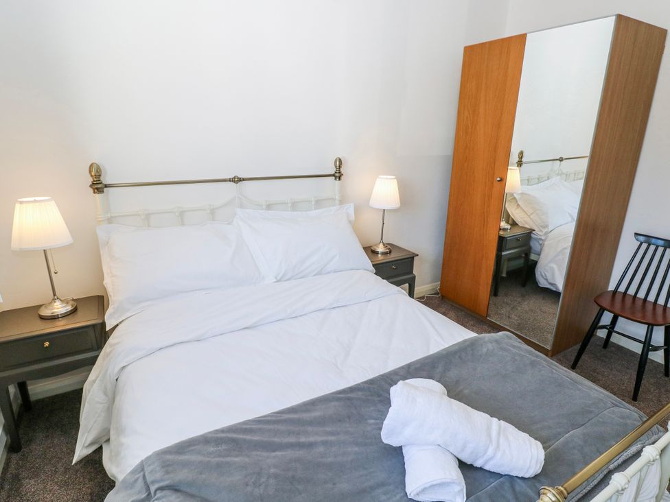 A bedroom with a bed, nightstand, lamp, and mirror at Moonraker in Saundersfoot