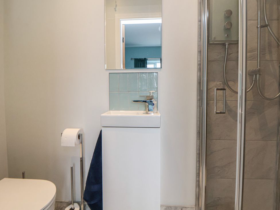 A bathroom with a sink, toilet, shower, and mirror at Mike’s Place in Rhyl
