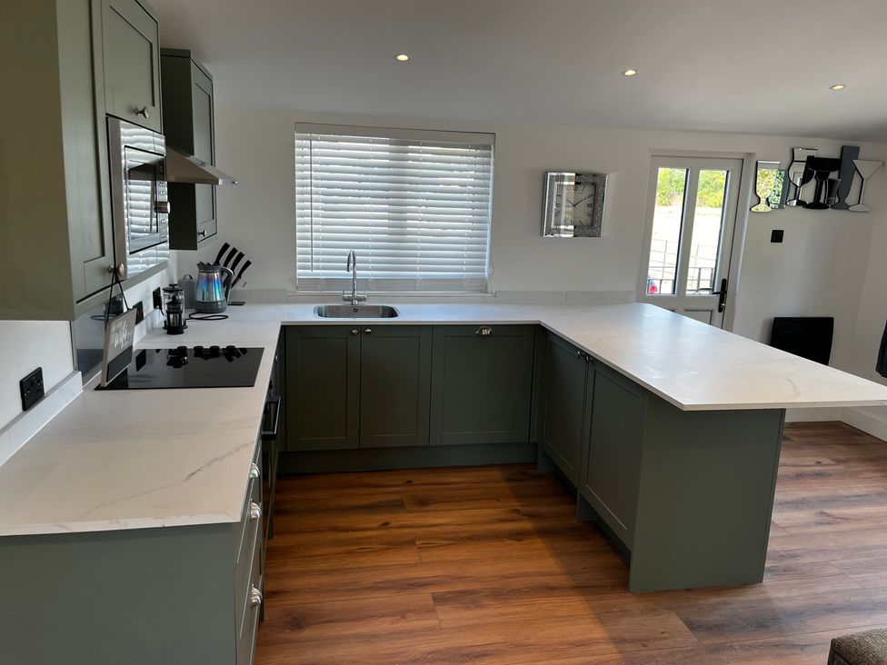 A kitchen with green units and a white countertop at Meadow View Cottage in Gloucester