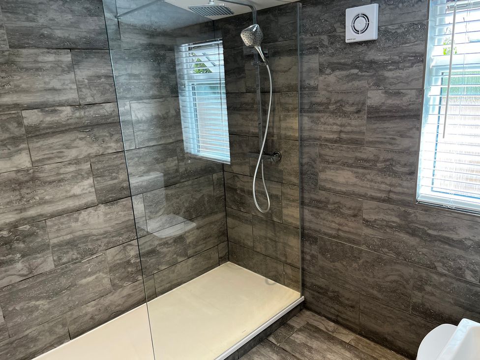 A shower area with glass door and tiled walls at Meadow View Cottage in Gloucester