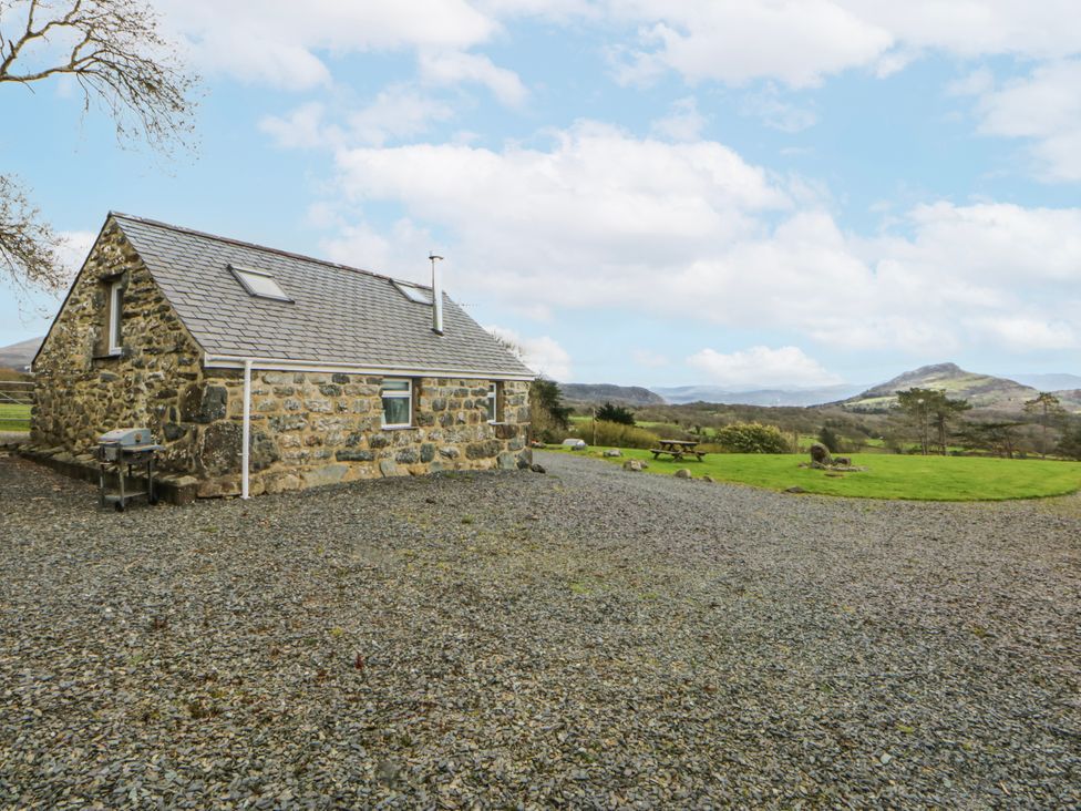 A stone house with gravel and a table at Little Barn near Criccieth