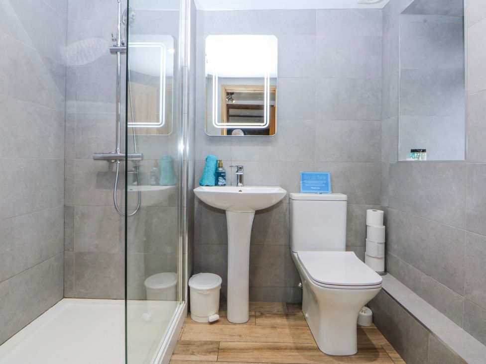 A bathroom with a shower, sink, toilet, and mirror at Little Barn near Criccieth