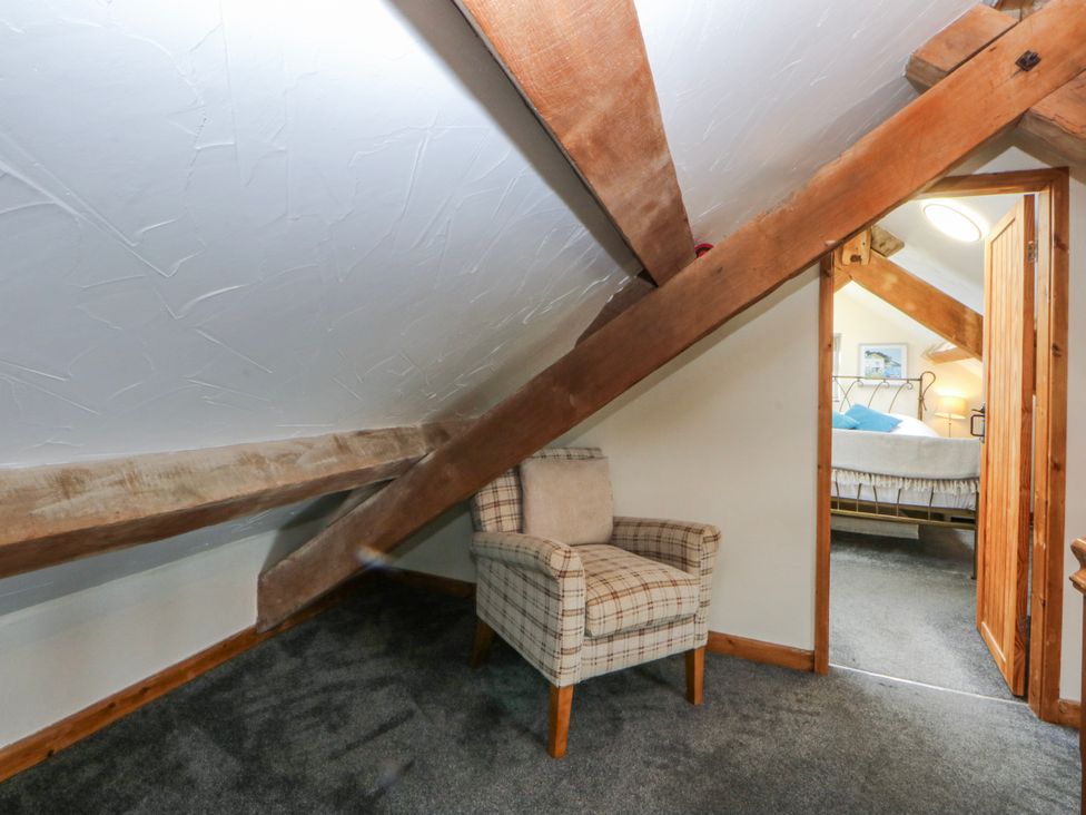 A bedroom with a chair and doorway leading to a bed at Little Barn near Criccieth