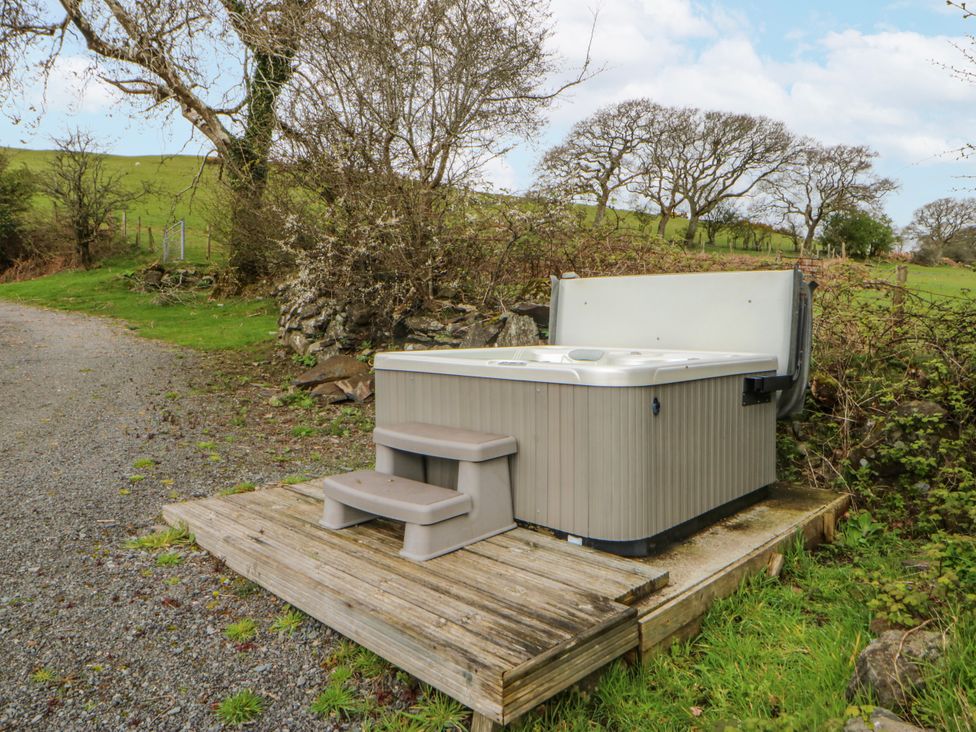 A hot tub on a wooden deck near a gravel path at Little Barn near Criccieth