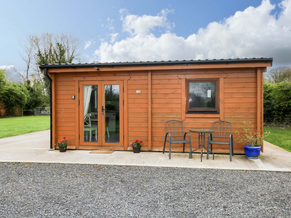 A log cabin with double doors and chairs on a patio at Nellies Log Cabin Kilcogy