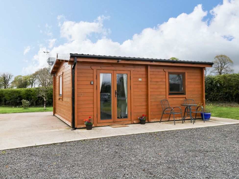 A wooden cabin with chairs and a table outside at Nellies Log Cabin in Kilcogy