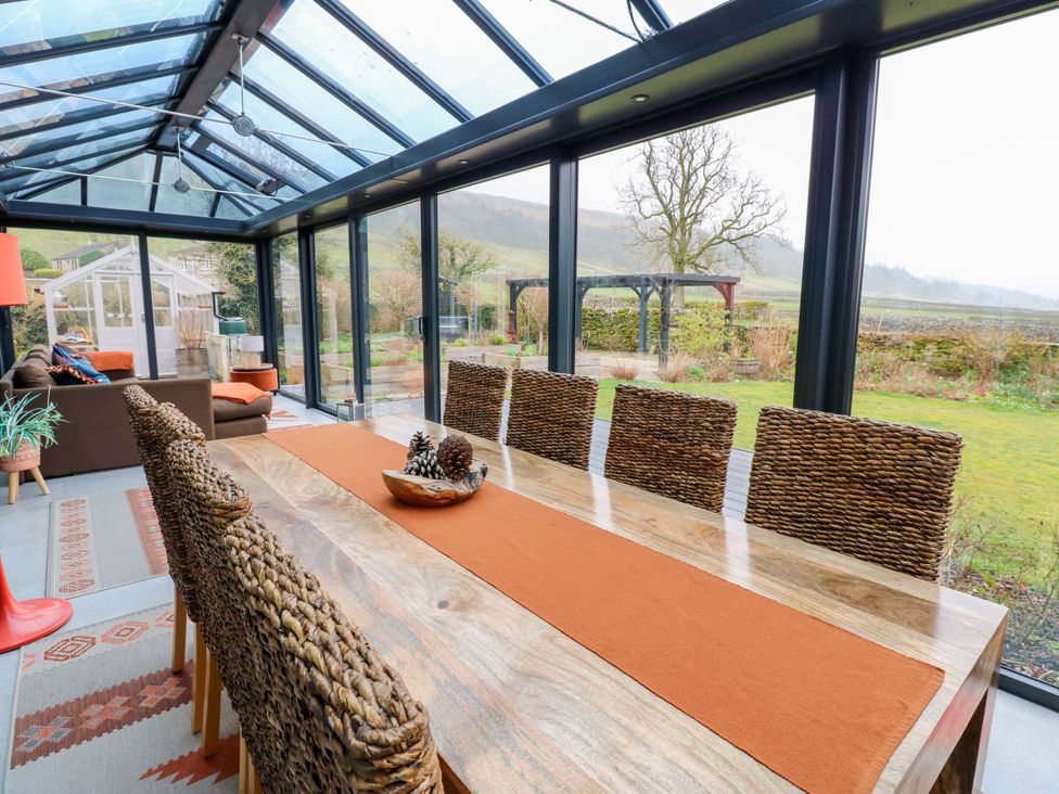 A conservatory with a dining table and chairs at Langcliffe House in Kettlewell