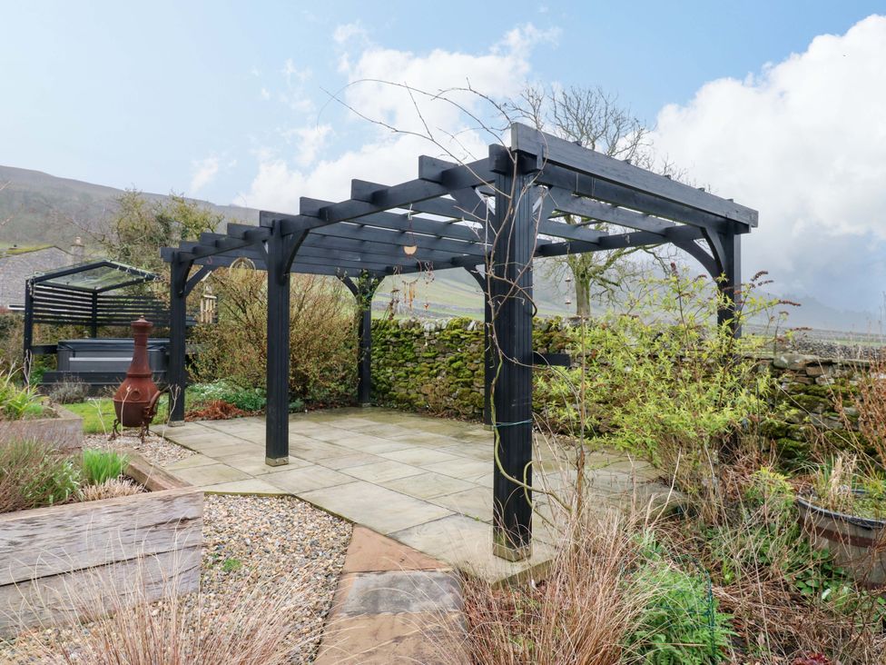 A garden with a pergola and stone wall at Langcliffe House in Kettlewell