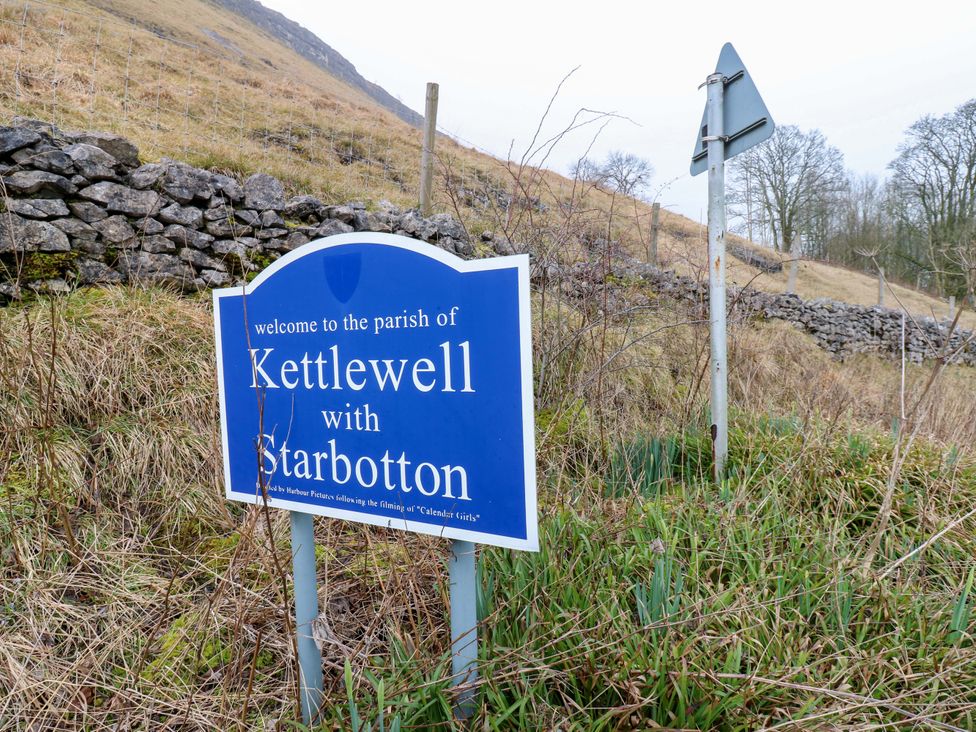 Welcome sign for Kettlewell with Starbotton near a stone wall and hill
