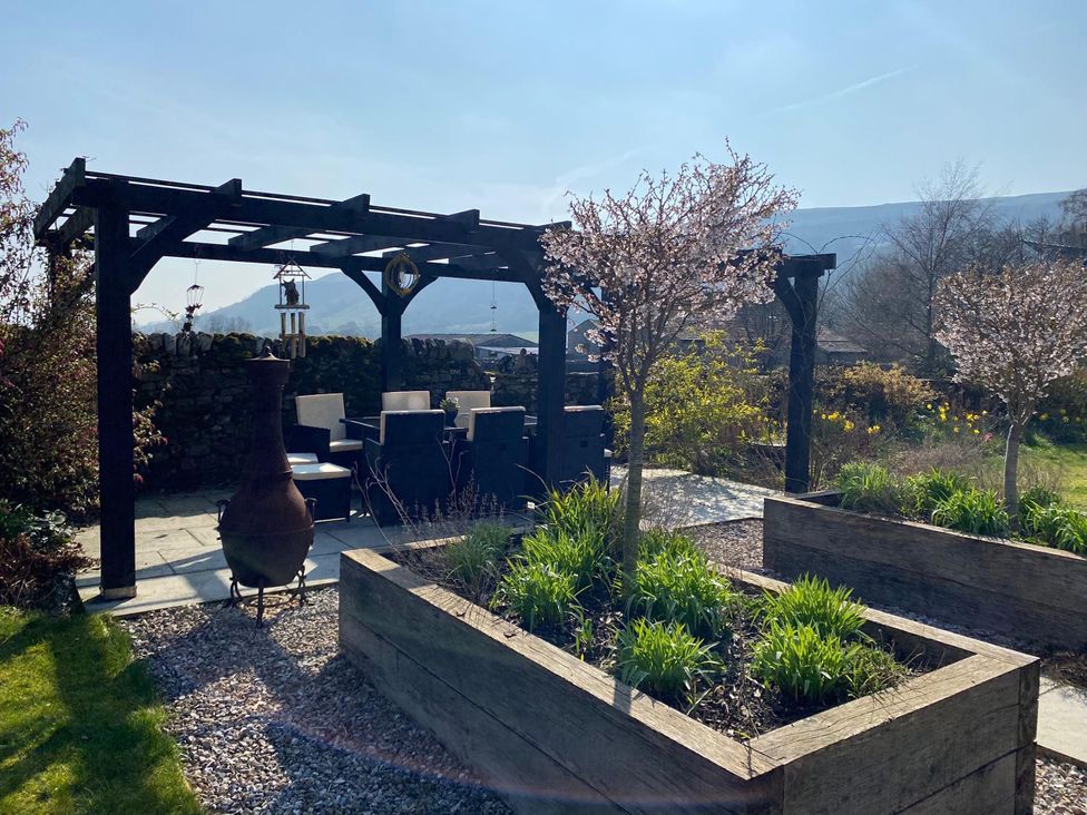 A garden with a pergola, chairs, and flowering trees at Langcliffe House Kettlewell