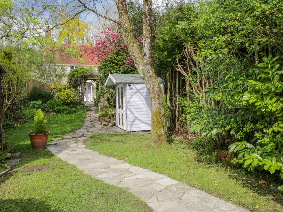 A garden with a stone pathway and a white shed at Lavender Cottage in Bourton, Dorset