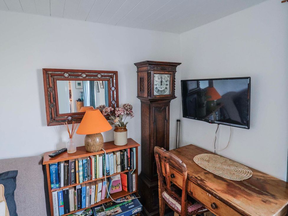 A living room with a clock, desk, lamp, and television at 2 Oak Tree Cottages Marshwood Nr. Hawkchurch