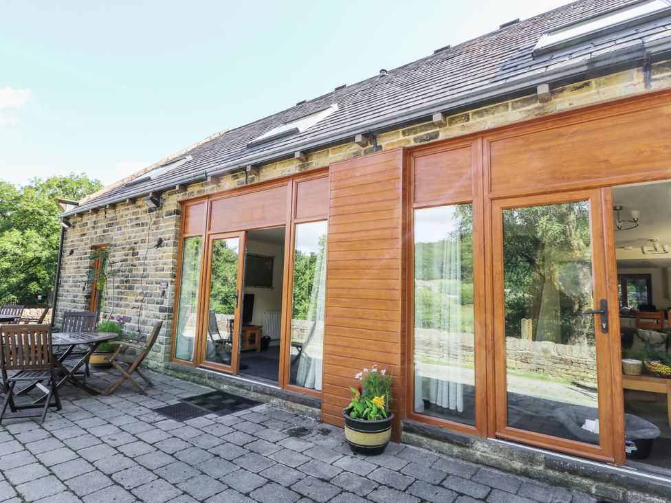 An outdoor patio with a wooden table and sliding doors at Victoria Wood View in Cragg Vale