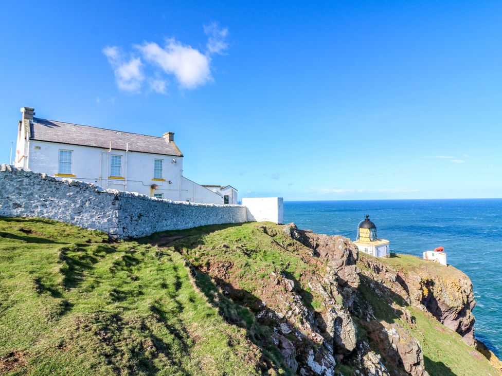 A house and lighthouse on a cliff by the sea at The Flaghouse at The Lighthouse St Abbs