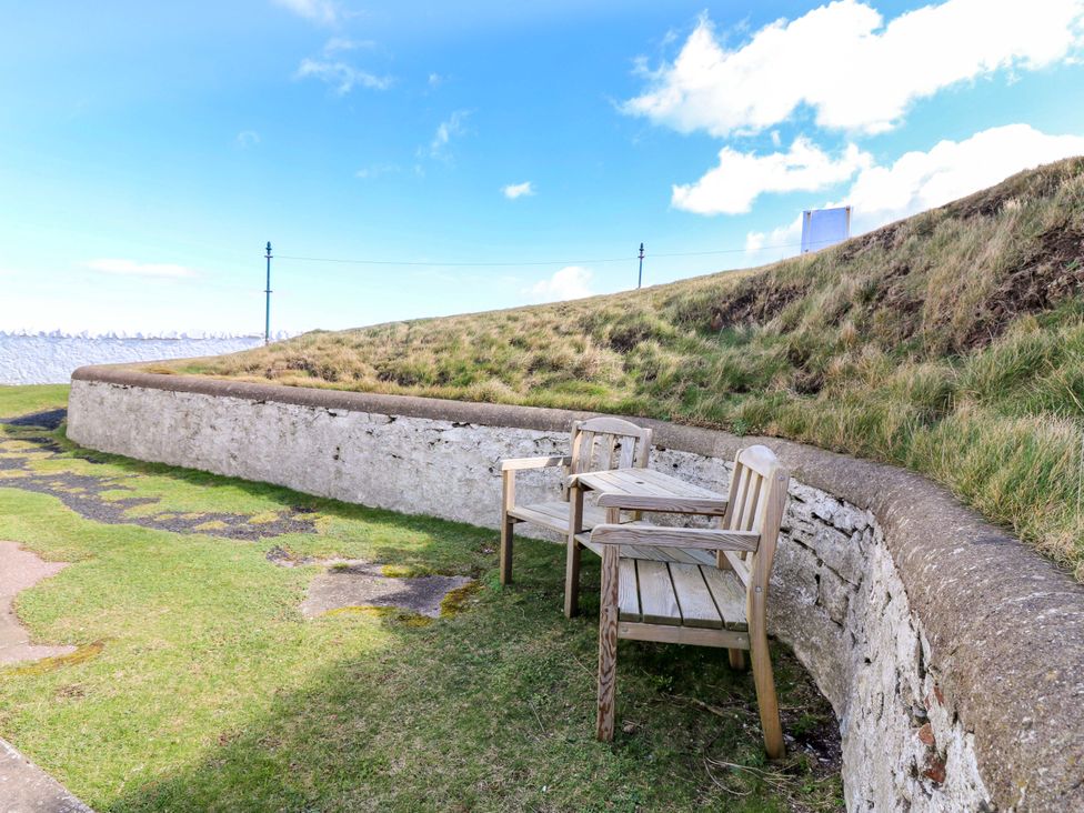 Two wooden chairs near a stone wall on a grassy area at The Flaghouse at The Lighthouse St Abbs