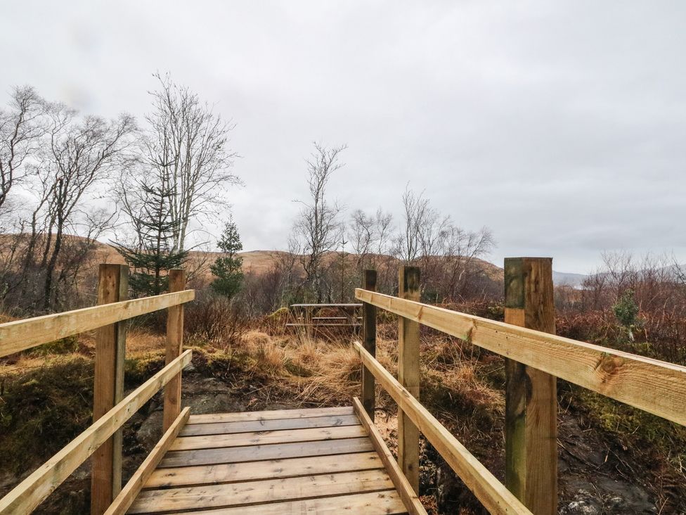A wooden bridge among trees with hills in the background at Doire An Daimh