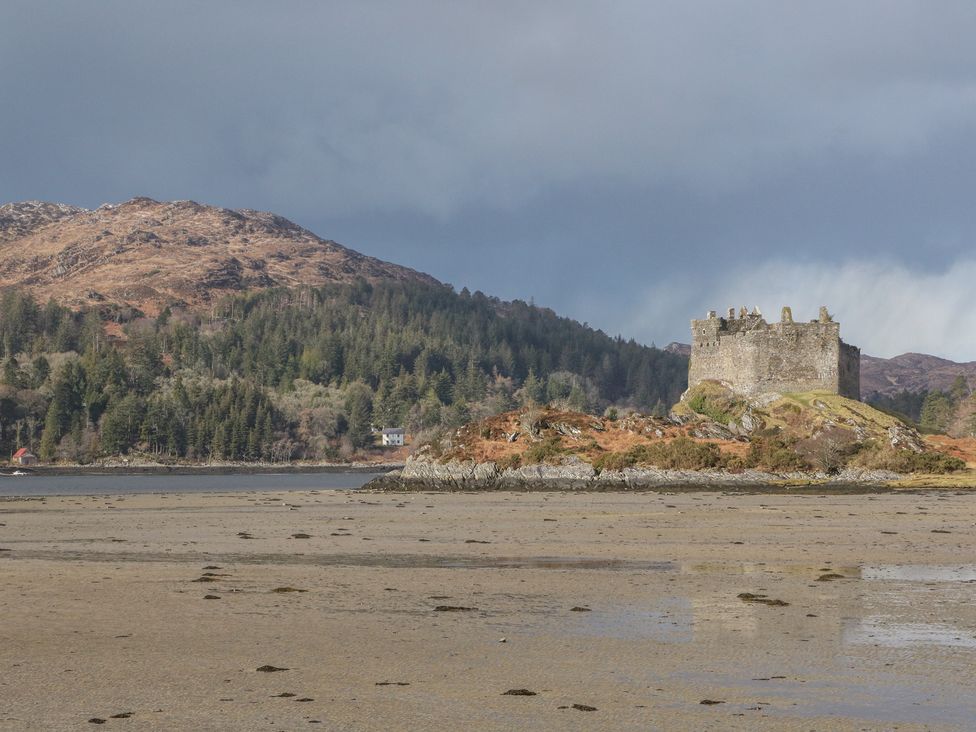 A castle on a rocky island with mountains and trees in the background at Doire An Daimh