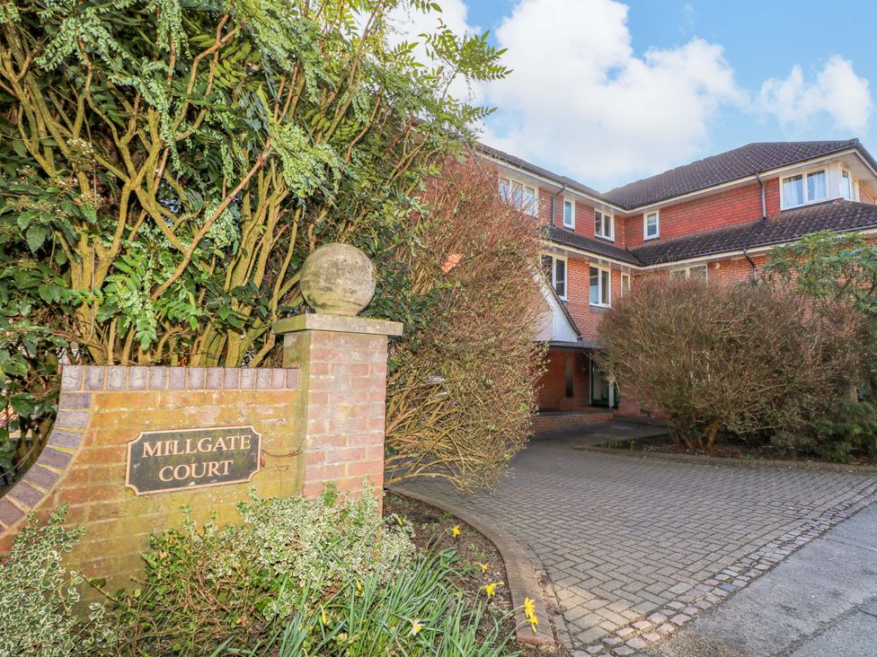 An outdoor area with a sign for Millgate Court and landscaped bushes near the entrance at Flat 16 in Farnham