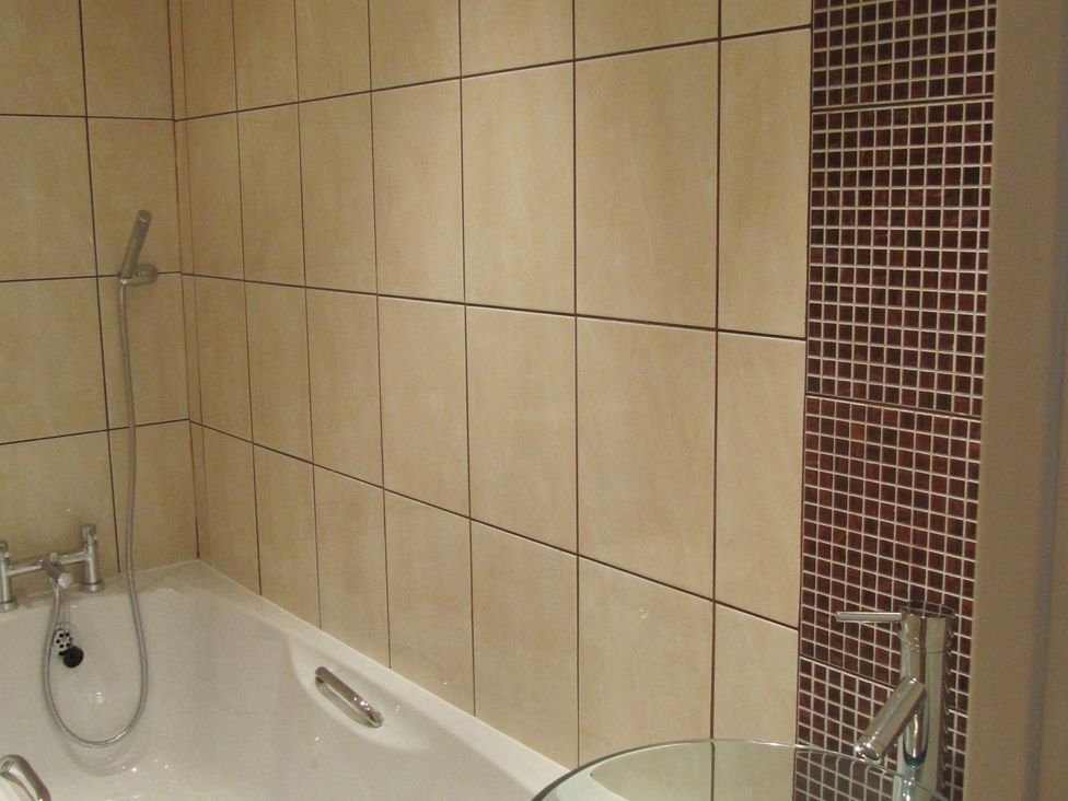 A bathtub with shower and tiled walls at Hope Cove near Kingsbridge