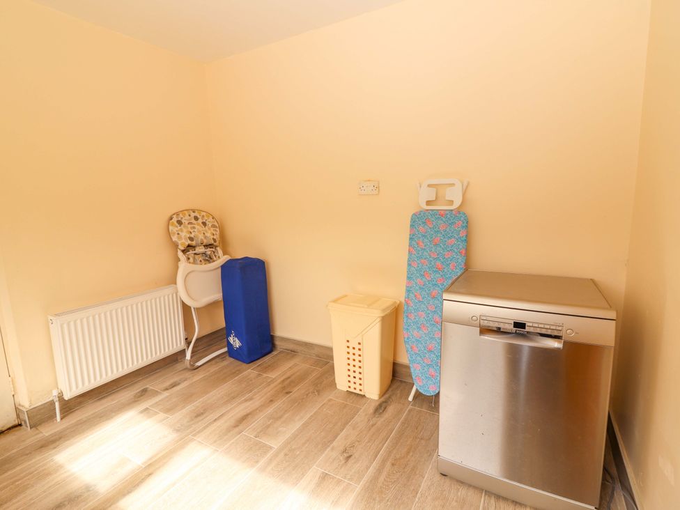 A utility room with a high chair, ironing board, basket, and dishwasher at Macmathuna, Kilrush, County Clare