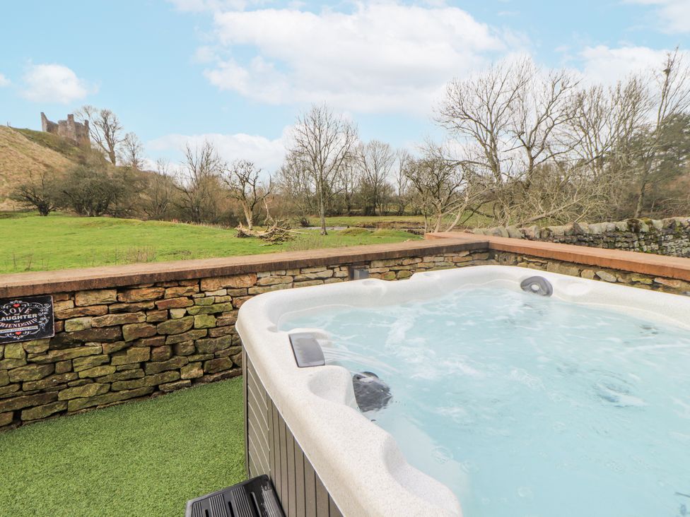 A hot tub with a stone wall and grassy area at Blue Heron Lodge in Kirkby Stephen