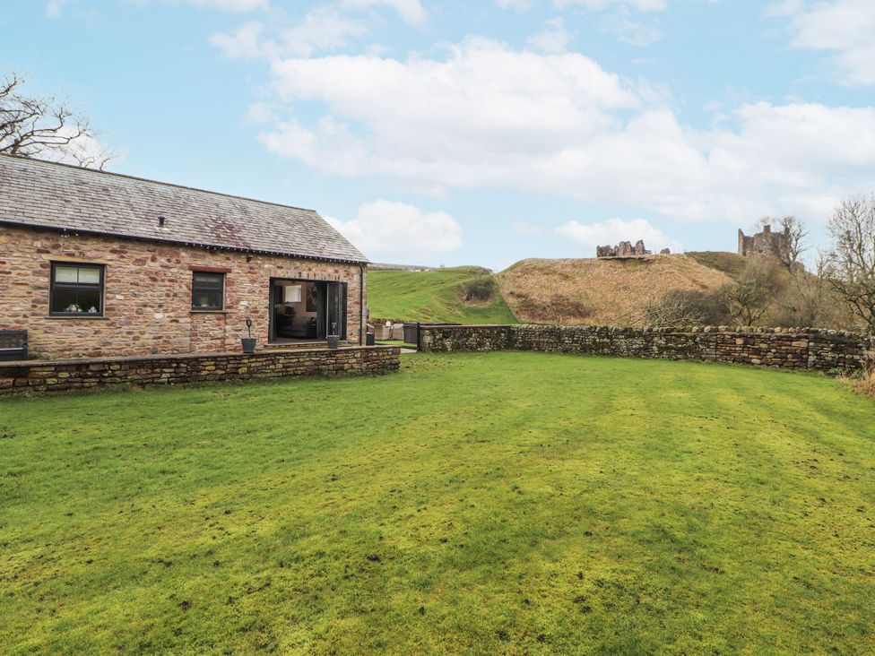 A garden with a stone house and lawn at Blue Heron Lodge in Kirkby Stephen