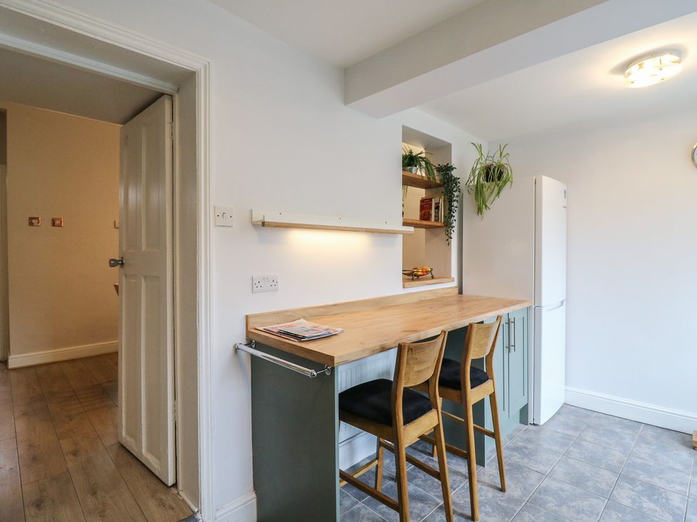 A kitchen with countertop, bar stools and refrigerator at Meregate Cottage in Margate