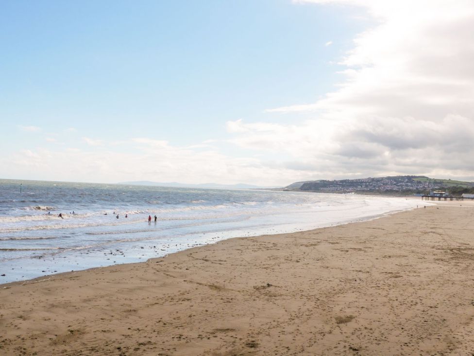 A beach with people walking along the shore at Gwynfa in Old Colwyn