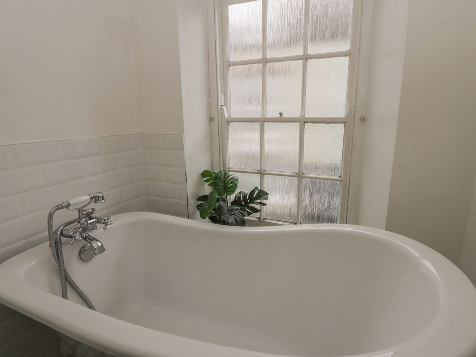 A bathroom with a bathtub and window at 1 Alpha Cottages in Tenby