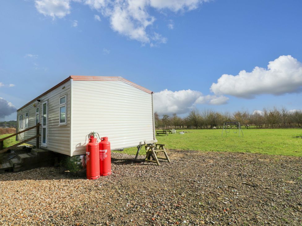 A caravan with gas cylinders and a swing set at Bengrove Wood Lodge in Shepton Mallet