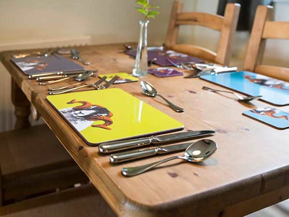 A dining room table set with cutlery and decorative placemats at Beacon Cottage in Ilkley