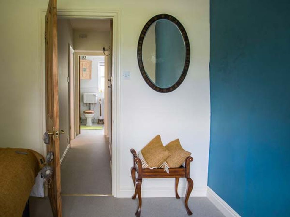 A hallway with a mirror and a stool at Beacon Cottage in Ilkley