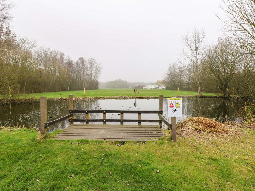 A pond with a wooden platform and a warning sign at the outdoor area of a caravan site in Great Yarmouth